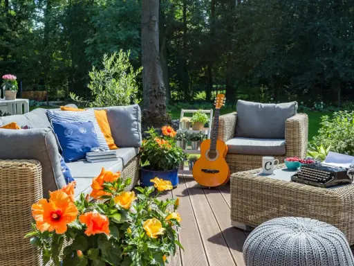 Przytulna aranżacja działki rekreacyjnej: rattanowe meble, gitara, kwiaty i maszyna do pisania tworzą idealne miejsce na relaks.
