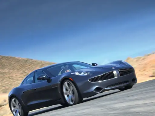 Elegancki, ciemnoszary Fisker Karma sunie po pustynnej drodze pod błękitnym niebem.