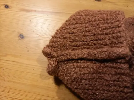 Bruna, sticka tovade tofflor ligger på ett träbord.