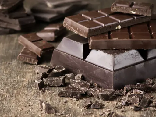 Des morceaux de chocolat noir, entiers et brisés, sur une table en bois. Une invitation à découvrir comment adoucir le chocolat noir pour une dégustation parfaite.