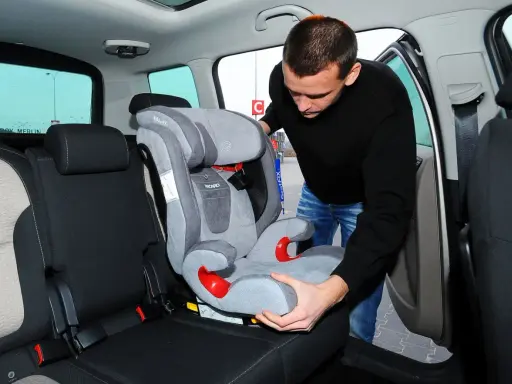Mężczyzna montuje fotelik dziecięcy, pokazując, jak zamontować isofix w aucie.