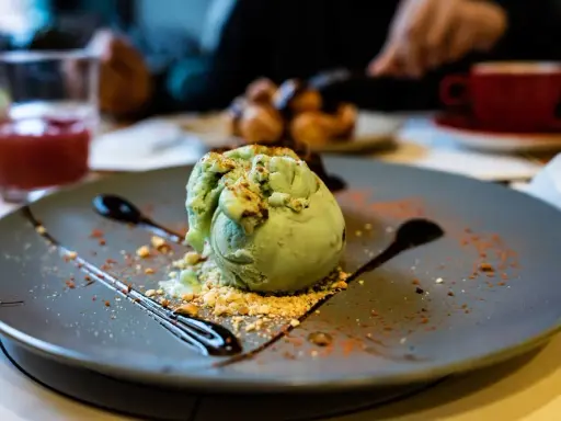 Pyszne lody pistacjowe na talerzu, ozdobione czekoladą i posypką. Idealny deser na poprawę humoru.