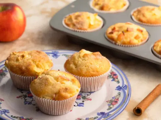 Frisch gebackene Apfelmuffins, die nach einem tollen apfelmuffins rezept duften. Daneben liegen Äpfel und Zimt.