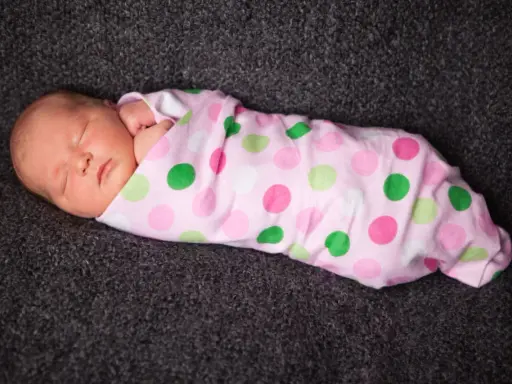 Schlafendes Baby, in rosa gepunktete Decke gewickelt. Pucken ja oder nein? Die süße Kleine scheint es zu mögen.