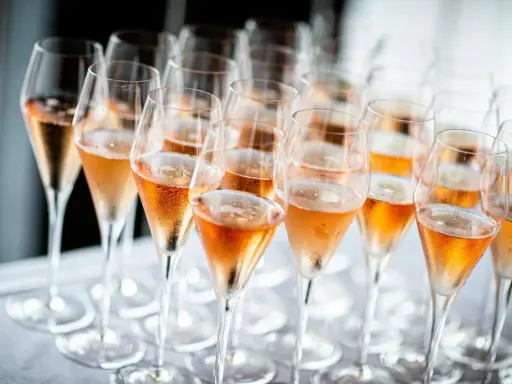 Reihe von Champagnergläsern mit Rosé-Champagner, bereit für den Genuss. So trinkt man Champagner: mit Stil und Freude.