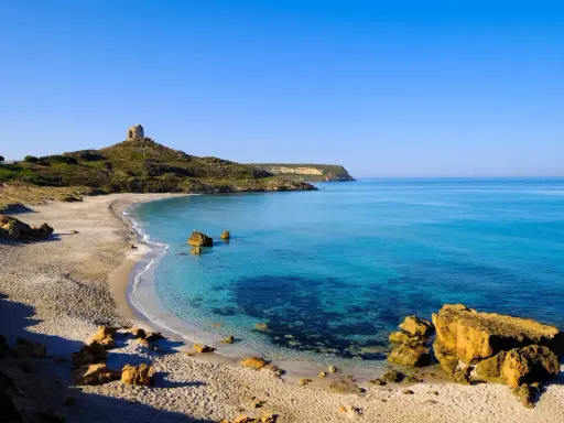Spiaggia dorata e mare cristallino in un'area marina protetta, con una torre antica su una collina.