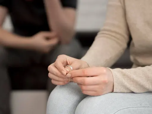 Dłoń kobiety trzyma obrączkę, symbol końca małżeństwa. Zastanawia się, jakie prawa ma niepracująca żona w takiej sytuacji.