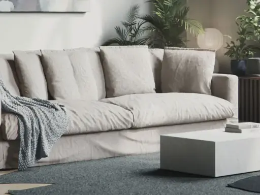En bekväm soffa med nedsuttna dynor, prydd med en stickad pläd. Framför står ett lågt, vitt soffbord.