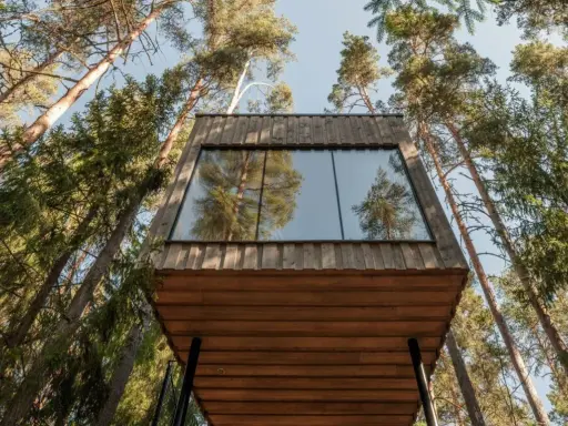 Ett modernt **wood hotel** i en svensk skog, med stora fönster som speglar träden.