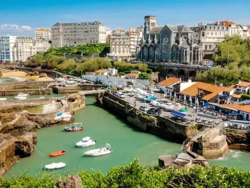 En vacker vy över hamnen i Biarritz med båtar i vattnet och en kyrka i bakgrunden. Kanske är det här tåg till Biarritz tar dig.