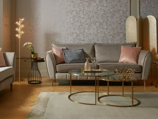 Przytulny salon glamour z beżową kanapą, różowymi poduszkami i złotymi dodatkami.