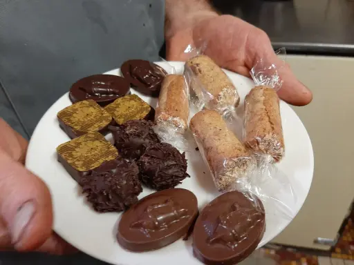 Assortiment de chocolats et biscuits, dont une spécialité d'Alençon, présentés sur une assiette blanche.