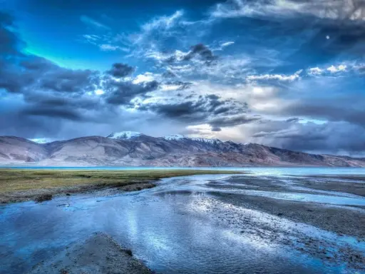 Paesaggio montano con lago e fiume, cielo drammatico con nuvole scure e luna, effetto HDR.