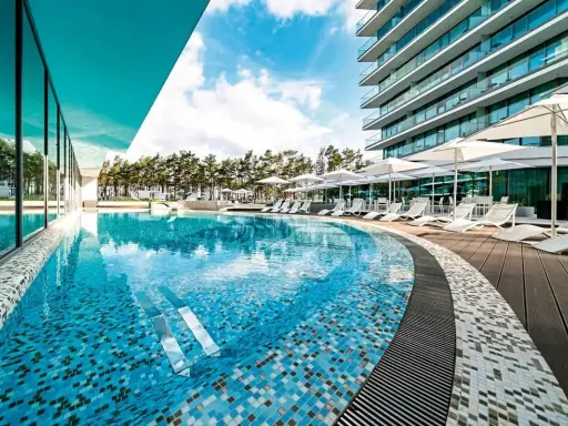 Luksusowy basen z mozaiką i leżakami, otoczony sosnami, przy nowoczesnym hotelu. Idealne miejsce na relaks, jak na plaży w Międzyzdrojach.