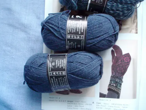 Two balls of dark blue yarn and a knitted glove with a floral pattern.