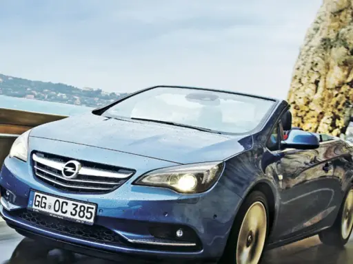 Niebieski Opel Cascada z opuszczonym dachem jedzie po mokrej drodze przy skalistym wybrzeżu.