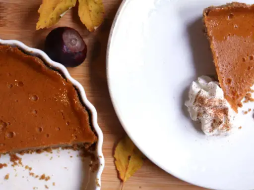 La tarta de calabaza de la abuela, con su relleno cremoso y corteza dorada, lista para ser disfrutada. Una rebanada servida con nata montada y canela.