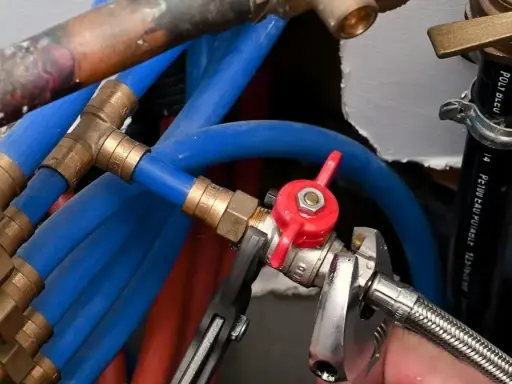 Réglage de la vanne arrivée d'eau maison avec une clé. Tuyaux bleus et rouges, raccords en laiton.