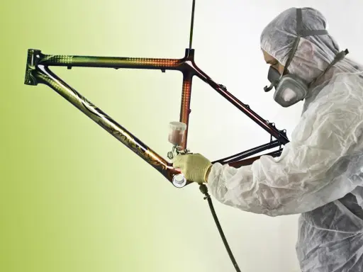 Person in Schutzanzug lackiert kunstvoll einen Rennrad Rahmen mit Spraydose.