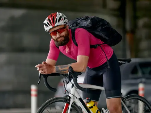 Mężczyzna w różowej koszulce i czarnych spodenkach rowerowych, kasku i okularach. Idealny strój, gdy zastanawiasz się, jak się ubrać na rower 15 stopni.