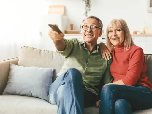 Uśmiechnięta para seniorów ogląda telewizję. Zastanawiają się, od jakiego wieku nie płaci się abonamentu RTV, ciesząc się wspólnym czasem.