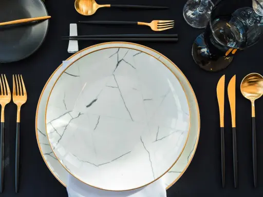 Service à la française définition : une table élégante avec des assiettes marbrées, des couverts dorés et noirs, et des verres sombres.