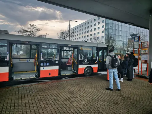 Buss vid flygplatsen, redo att ta resenärer från prag flygplats till centrum. En modern byggnad syns i bakgrunden.