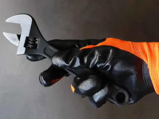 Mano enguantada sujeta llave inglesa ajustable, herramienta esencial para saber para que sirve la llave inglesa al apretar o aflojar tuercas y tornillos.