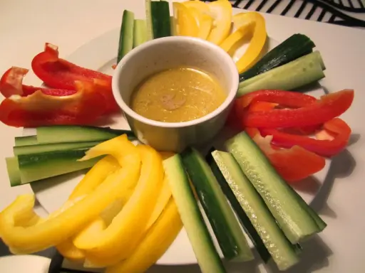 En skål med bagna cauda-sås omgiven av färgglada grönsaksstavar: röd och gul paprika samt gurka.
