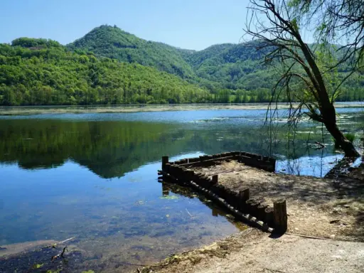 Un pontile in legno sul lago di Fimon, circondato da colline verdi e alberi.
