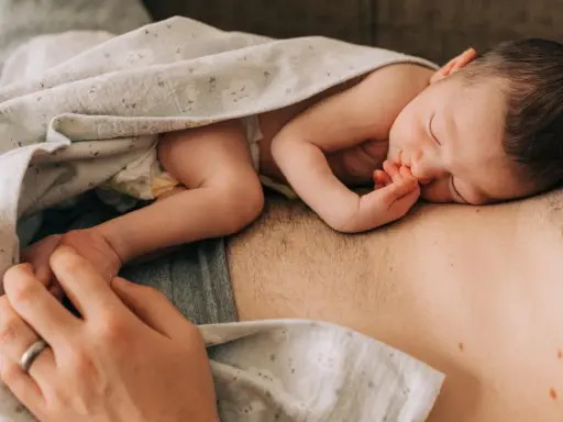 Ein Neugeborenes schläft auf der Brust seines Vaters. Die Frage "wie werde ich ein guter vater" wird hier durch diese liebevolle Szene beantwortet.