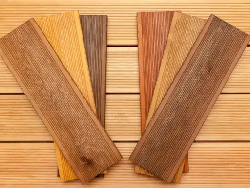 Verschiedene Holzproben mit unterschiedlichen Farben und Maserungen liegen auf einer Holzoberfläche. Sie zeigen die Vielfalt der dauerhaftigkeitsklassen holz für Terrassendielen.