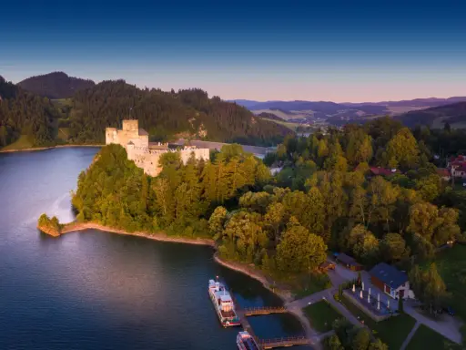 Zamek w Niedzicy nad jeziorem, otoczony zielenią, w malowniczej scenerii Pienińskiego Parku Narodowego.