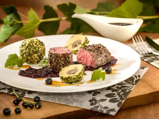 Edles Fleischgericht mit Johannisbeeren verwerten: zartes Rinderfilet, umhüllt von Kräutern und Nüssen, serviert mit einer fruchtigen Johannisbeersauce und Beilagen.