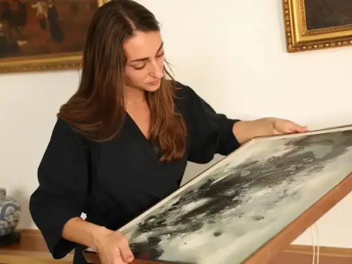Une femme examine un tableau abstrait, cherchant des indices pour comment estimer un tableau avec signature.