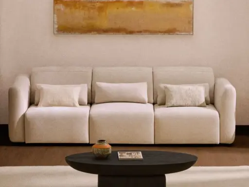 Sofá beige con cojines, mesa de centro oscura, alfombra clara y cuadro abstracto. Los colores feng shui crean un ambiente sereno.