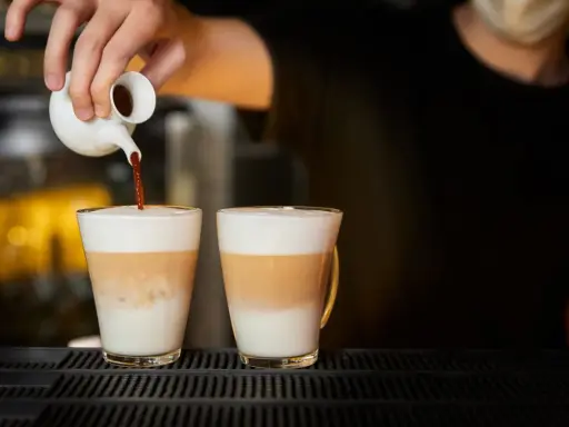 Barista wlewa espresso do dwóch latte macchiato. Zastanawiasz się, ile kcal ma latte macchiato?