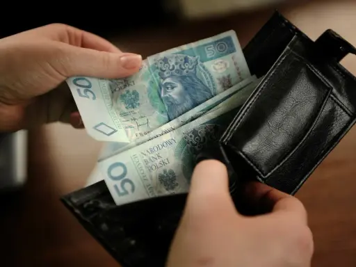 Ręce wkładają polskie banknoty 50 zł do czarnego portfela. To kieszonkowe dla dziecka na drobne wydatki.