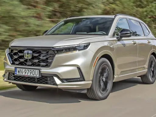 Nowy Honda CR-V w kolorze złotym jedzie po drodze, otoczony zielenią.