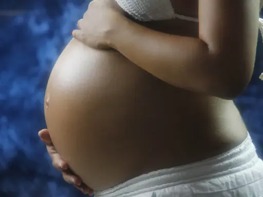 Pancia di donna incinta, con mani che la accarezzano. Si intravede un bikini bianco e uno sfondo blu. L'addome è tonico, forse con un leggero intestino iperecogeno visibile.