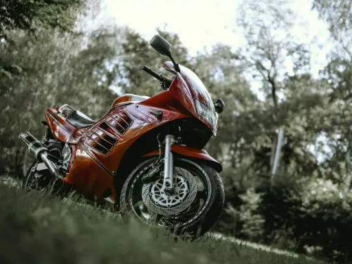 Czerwony motocykl Suzuki RF 900, zaparkowany na trawie wśród drzew. Idealny do sprawdzenia jego danych technicznych.