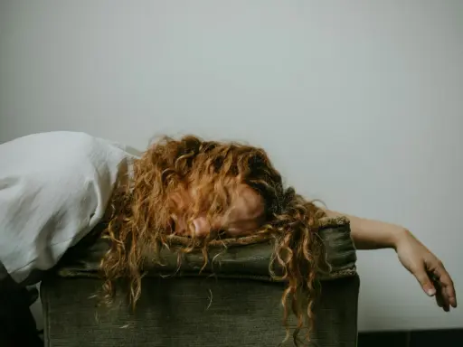 Donna con capelli rossi ricci, viso nascosto, sembra sopraffatta, forse un attacco di panico o uno svenimento.