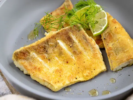 Zanderfilet ohne Haut braten: goldbraune Fischfilets auf grauem Teller, garniert mit Dill und Limettenspalten.
