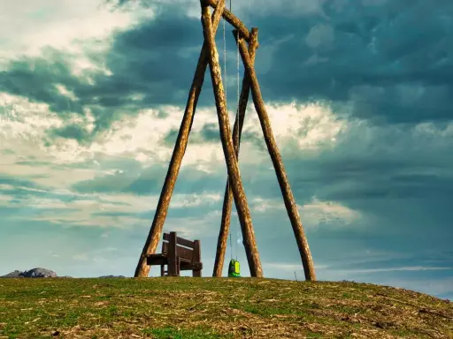 Un columpio ríachuelo solitario en la cima de una colina, con un banco y una mochila verde, bajo un cielo dramático.