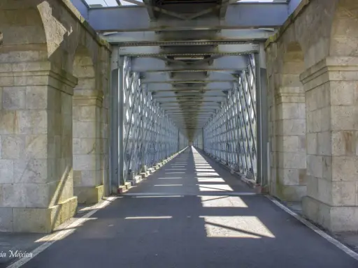 El **puente internacional Tui** se alza imponente, un túnel de metal y piedra que se pierde en la distancia, proyectando sombras geométricas sobre el asfalto.