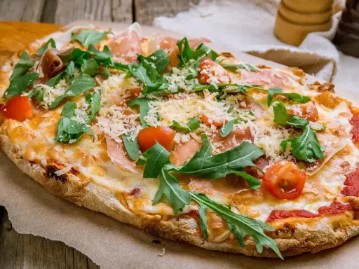 Eine leckere Pinsa belegen mit Schinken, Rucola und Kirschtomaten. Käse und Tomatensauce runden den Genuss ab.