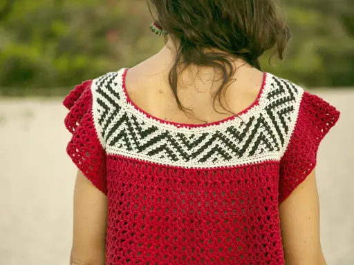 Detalle de un top de ganchillo rojo con un patrón geométrico blanco y negro en el cuello.