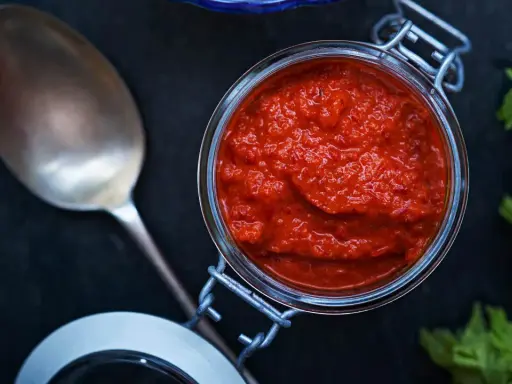 En burk med kryddig mojo rojo bredvid en sked och selleri. Perfekt för att ge smak till maten.