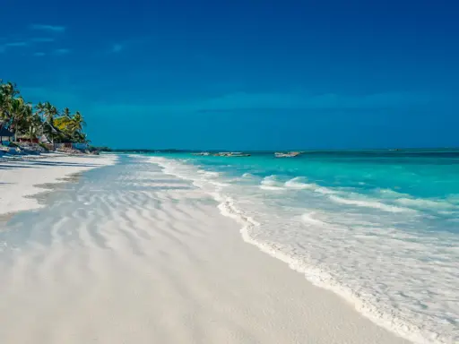 En vit sandstrand med turkost vatten och palmer vid Kendwa, Zanzibar. Båtar guppar i fjärran.