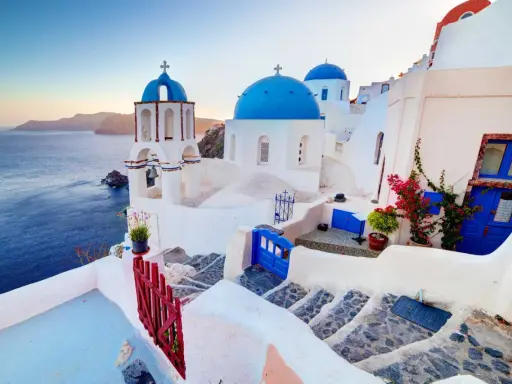 Białe domy z niebieskimi kopułami kościołów na tle morza i wysp. Widok na kaldera Santorini o zachodzie słońca.